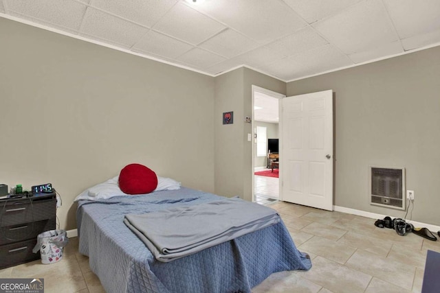 bedroom with heating unit, a drop ceiling, ornamental molding, and light tile patterned flooring