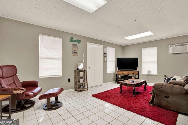 living room featuring a drop ceiling, light tile patterned floors, and a wall mounted air conditioner