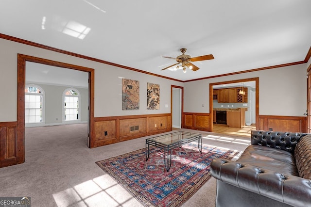 living room with ceiling fan, wood walls, light colored carpet, and crown molding