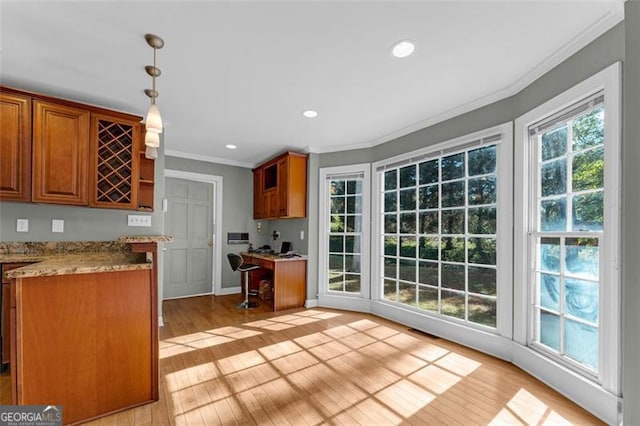 kitchen featuring pendant lighting, light stone counters, crown molding, and light hardwood / wood-style flooring