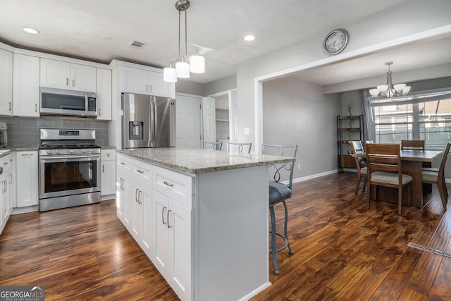 kitchen with a center island, white cabinets, stainless steel appliances, and decorative light fixtures