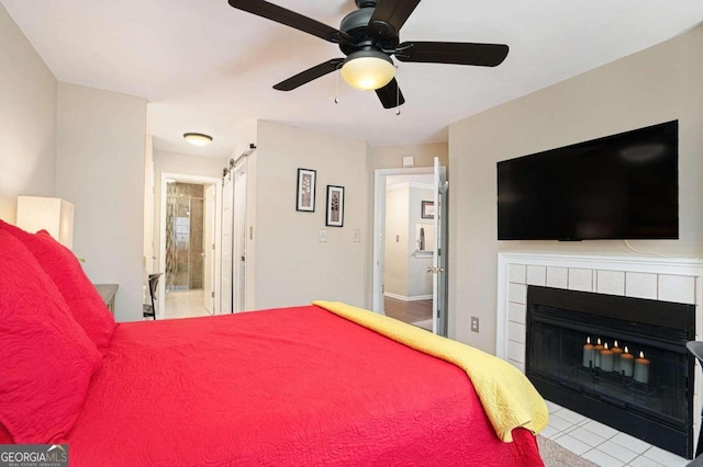 bedroom with ceiling fan, a barn door, a tiled fireplace, connected bathroom, and light tile patterned flooring