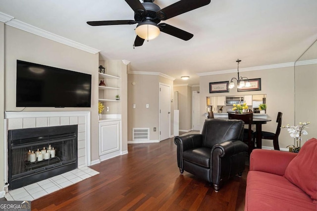 living room featuring dark hardwood / wood-style floors, ceiling fan, crown molding, and a tile fireplace