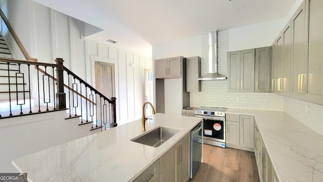 kitchen featuring appliances with stainless steel finishes, sink, decorative backsplash, light stone countertops, and wall chimney range hood