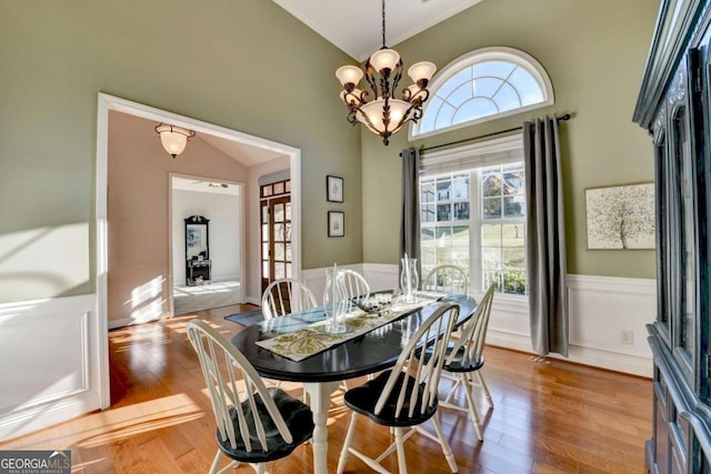 dining room with a healthy amount of sunlight, a chandelier, vaulted ceiling, and light hardwood / wood-style flooring