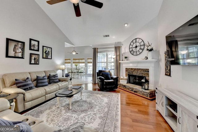 living room featuring high vaulted ceiling, a stone fireplace, and light hardwood / wood-style floors