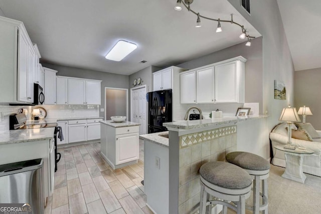 kitchen featuring black appliances, white cabinetry, a breakfast bar area, a center island, and kitchen peninsula