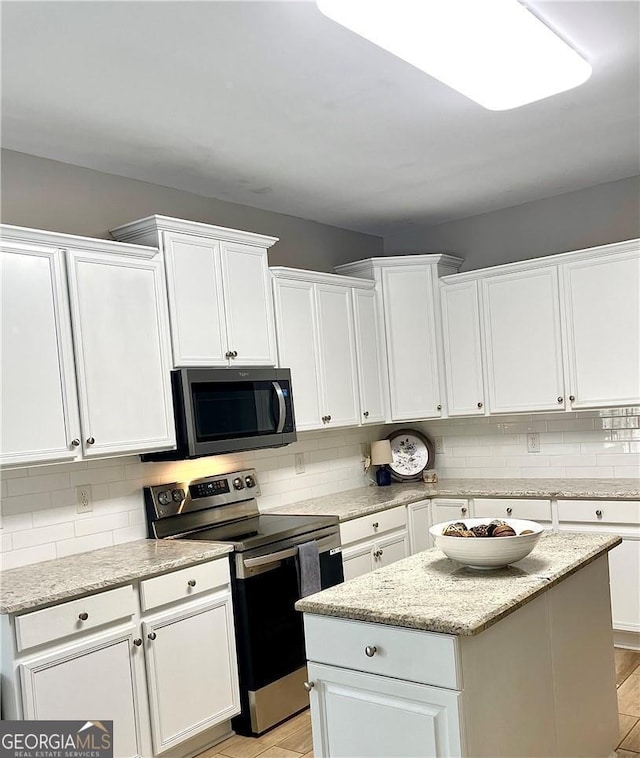 kitchen with white cabinetry, light stone counters, a kitchen island, and appliances with stainless steel finishes