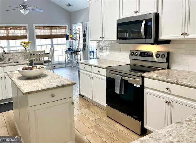 kitchen featuring vaulted ceiling, appliances with stainless steel finishes, white cabinetry, sink, and light stone countertops