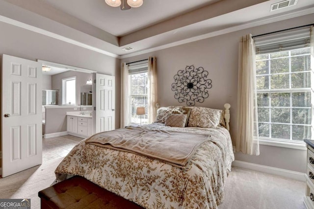 bedroom featuring connected bathroom, light colored carpet, and a raised ceiling