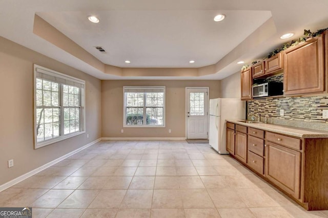 kitchen featuring a raised ceiling, sink, light tile patterned floors, and backsplash