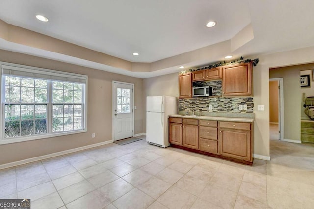 kitchen featuring sink, backsplash, white refrigerator, light tile patterned floors, and a raised ceiling