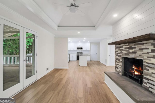 unfurnished living room featuring ceiling fan, a raised ceiling, crown molding, light wood-type flooring, and french doors