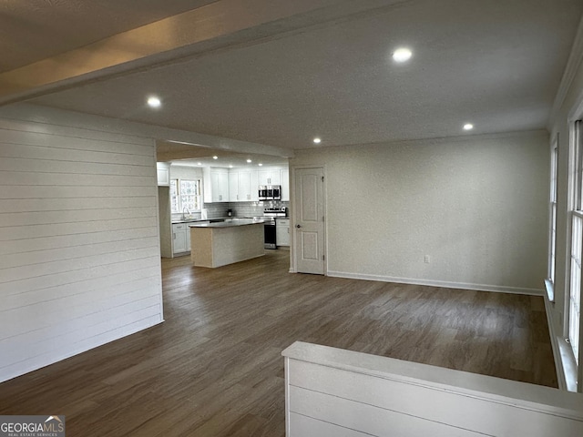 unfurnished living room featuring dark wood finished floors, recessed lighting, a sink, beamed ceiling, and baseboards