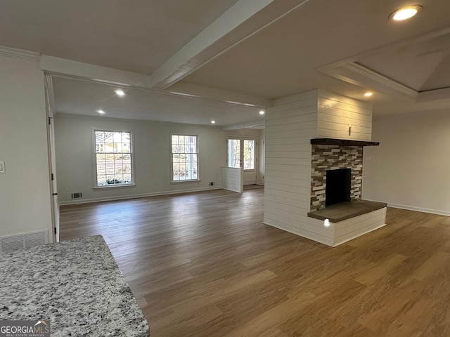 unfurnished living room with visible vents, plenty of natural light, a stone fireplace, and wood finished floors