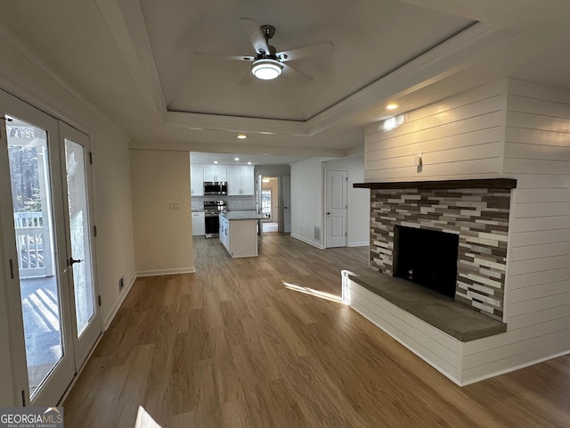 unfurnished living room with baseboards, ornamental molding, wood finished floors, a tray ceiling, and a fireplace