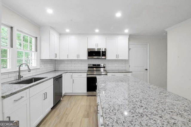 kitchen with appliances with stainless steel finishes, white cabinetry, sink, backsplash, and light stone counters