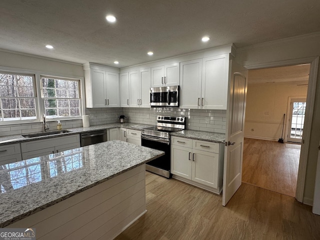 kitchen featuring light wood-style floors, appliances with stainless steel finishes, a sink, and ornamental molding