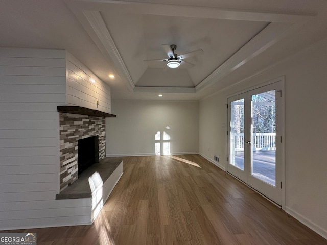 unfurnished living room featuring a fireplace with raised hearth, a raised ceiling, ceiling fan, wood finished floors, and french doors