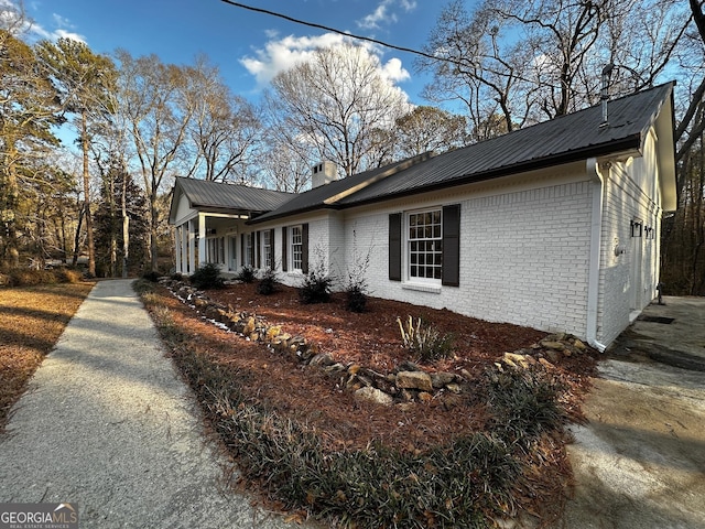 view of side of property featuring a chimney, metal roof, and brick siding