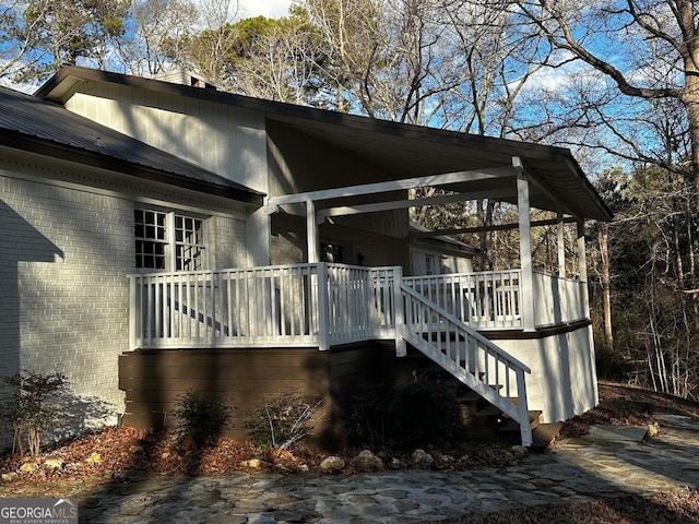 view of side of home featuring brick siding, metal roof, stairway, and a wooden deck