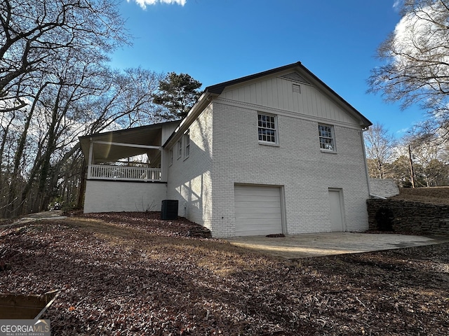 view of side of property with central AC, brick siding, board and batten siding, and an attached garage