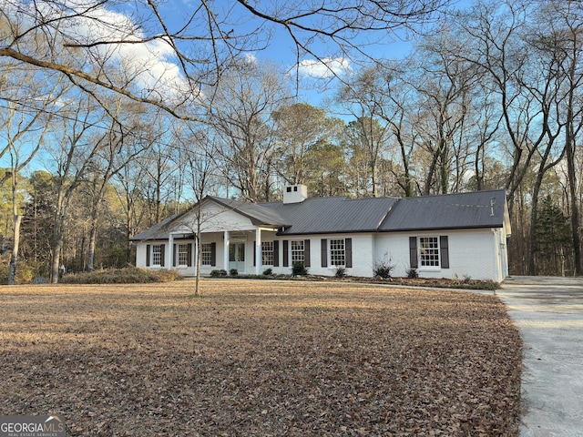 view of front facade with brick siding, metal roof, a chimney, and a front lawn