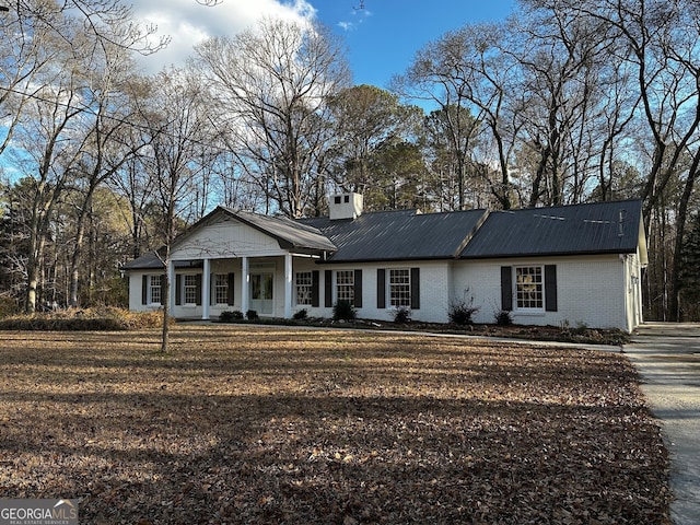 view of front facade featuring metal roof, brick siding, a chimney, and a front lawn