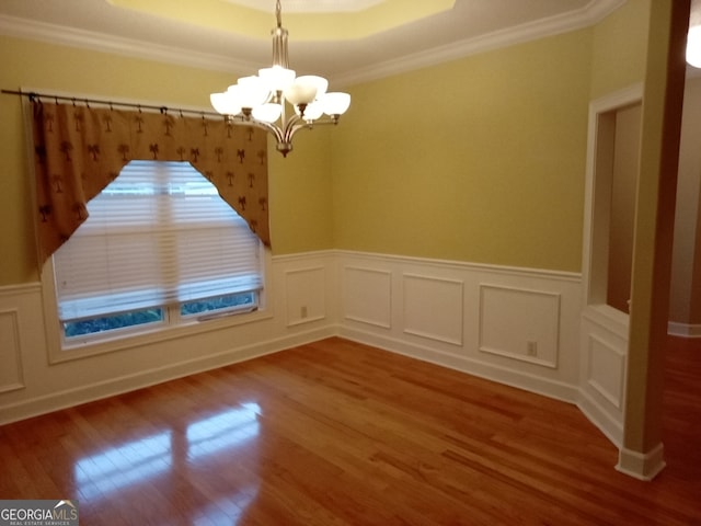 unfurnished dining area with hardwood / wood-style floors, ornamental molding, a tray ceiling, and a chandelier