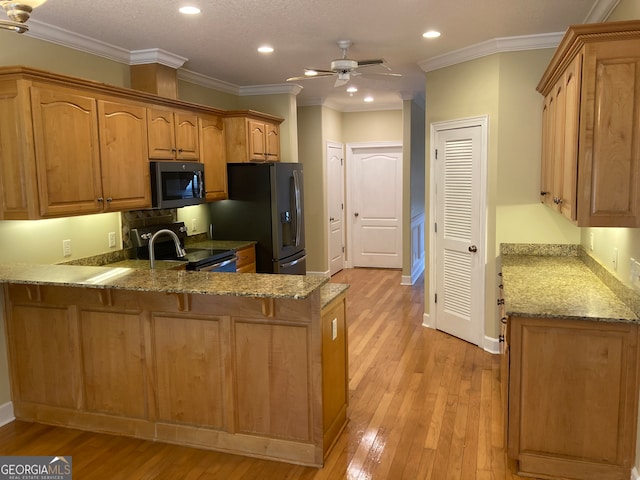 kitchen with ornamental molding, stainless steel appliances, light stone counters, and light hardwood / wood-style floors