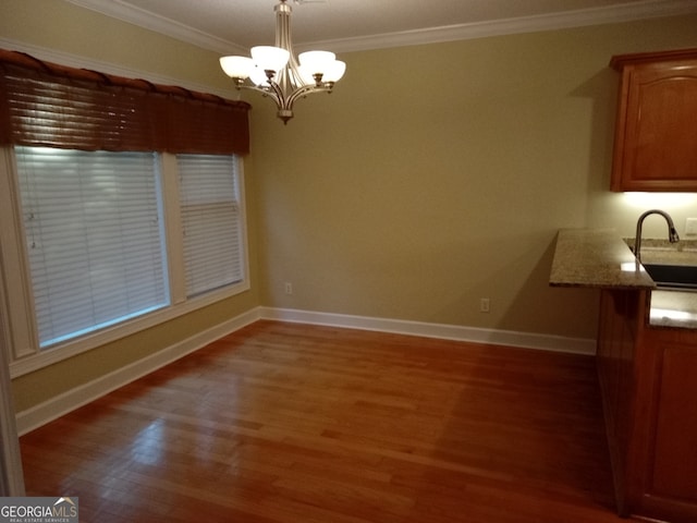 unfurnished dining area with wood-type flooring, an inviting chandelier, crown molding, and sink