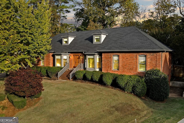 view of front of house with a yard, a shingled roof, and brick siding