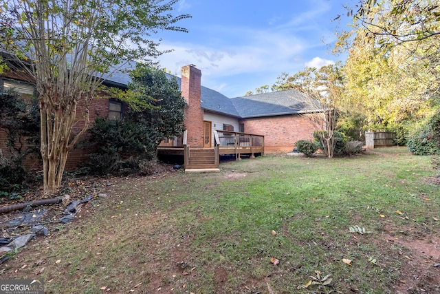 back of property with a deck, brick siding, a lawn, and a chimney