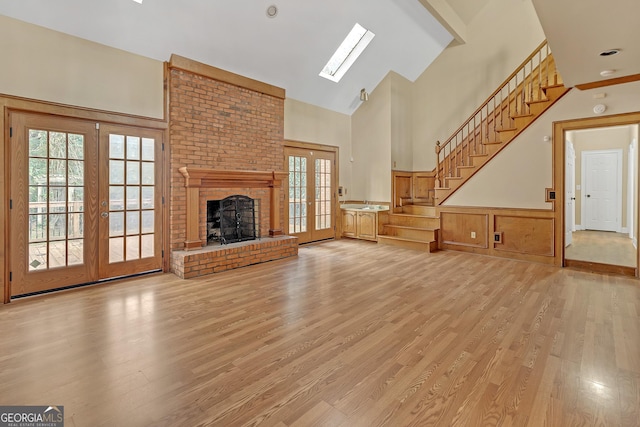 unfurnished living room featuring high vaulted ceiling, french doors, stairway, light wood-type flooring, and a brick fireplace