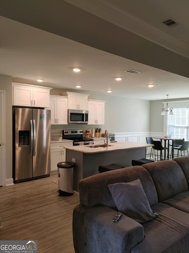 kitchen featuring white cabinetry, stainless steel appliances, an inviting chandelier, hardwood / wood-style floors, and a kitchen island with sink