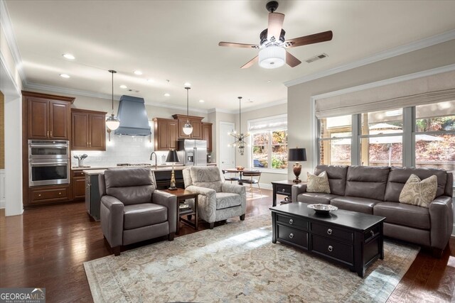 living room with crown molding, dark hardwood / wood-style flooring, and ceiling fan with notable chandelier