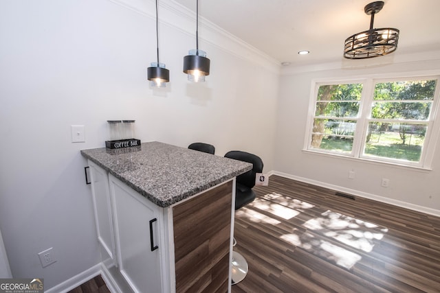 interior space featuring light stone countertops, dark wood-type flooring, pendant lighting, and ornamental molding