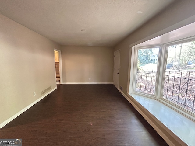 unfurnished room with a textured ceiling and dark wood-type flooring