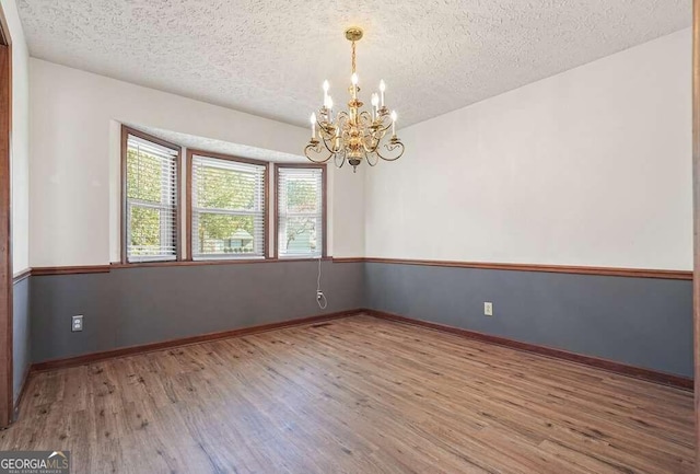 unfurnished room featuring an inviting chandelier, a textured ceiling, and light hardwood / wood-style flooring