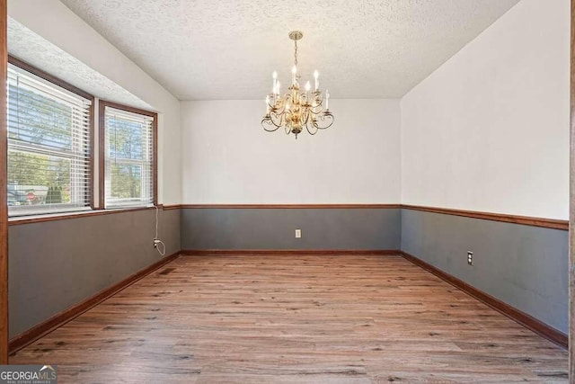 empty room with an inviting chandelier, a textured ceiling, and light wood-type flooring