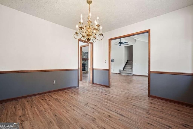 unfurnished room with ceiling fan with notable chandelier, a textured ceiling, and dark hardwood / wood-style floors