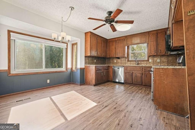 kitchen featuring pendant lighting, backsplash, light hardwood / wood-style flooring, stainless steel dishwasher, and a textured ceiling