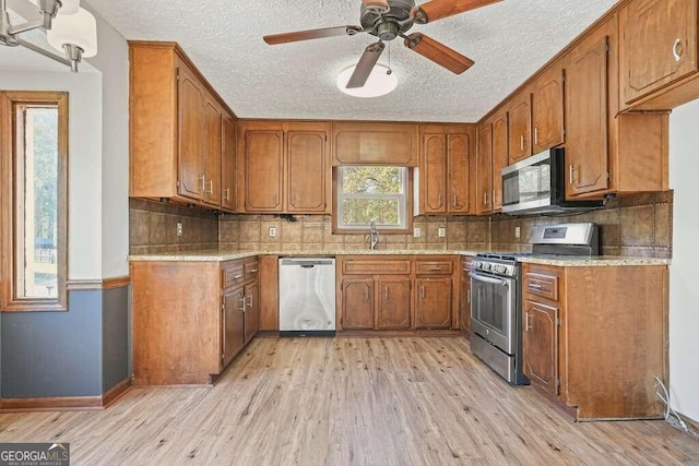 kitchen with backsplash, ceiling fan, light hardwood / wood-style floors, and appliances with stainless steel finishes