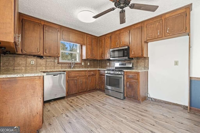 kitchen with backsplash, ceiling fan, light hardwood / wood-style flooring, and stainless steel appliances