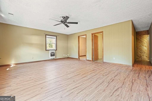 empty room featuring a textured ceiling, heating unit, ceiling fan, light hardwood / wood-style floors, and wood walls