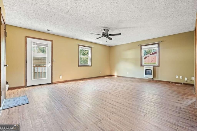 unfurnished room featuring a textured ceiling, light wood-type flooring, heating unit, and ceiling fan