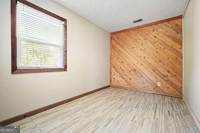 empty room with light hardwood / wood-style floors, a textured ceiling, and wooden walls