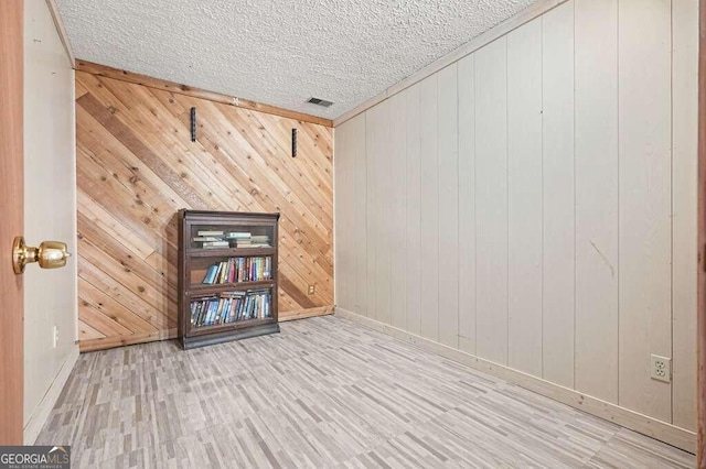 unfurnished room with a textured ceiling, light hardwood / wood-style flooring, and wood walls