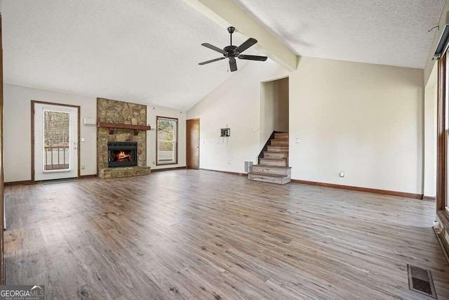 unfurnished living room with a textured ceiling, lofted ceiling with beams, hardwood / wood-style flooring, and a stone fireplace