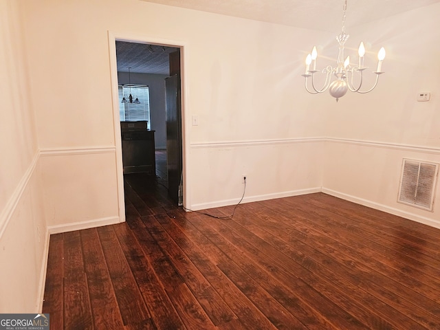 empty room featuring dark wood-type flooring and a notable chandelier